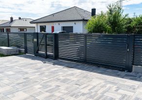 A modern panel fence in anthracite color, a visible sliding gate to the garage and a wicket with a letterbox.