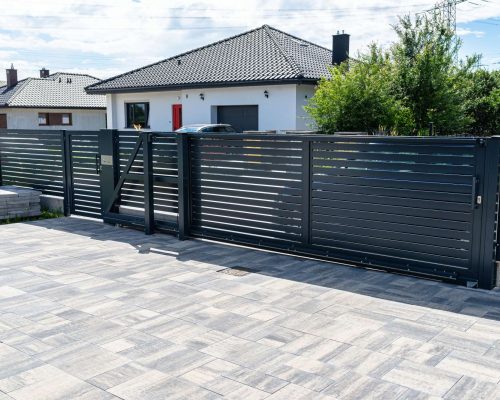 A modern panel fence in anthracite color, a visible sliding gate to the garage and a wicket with a letterbox.